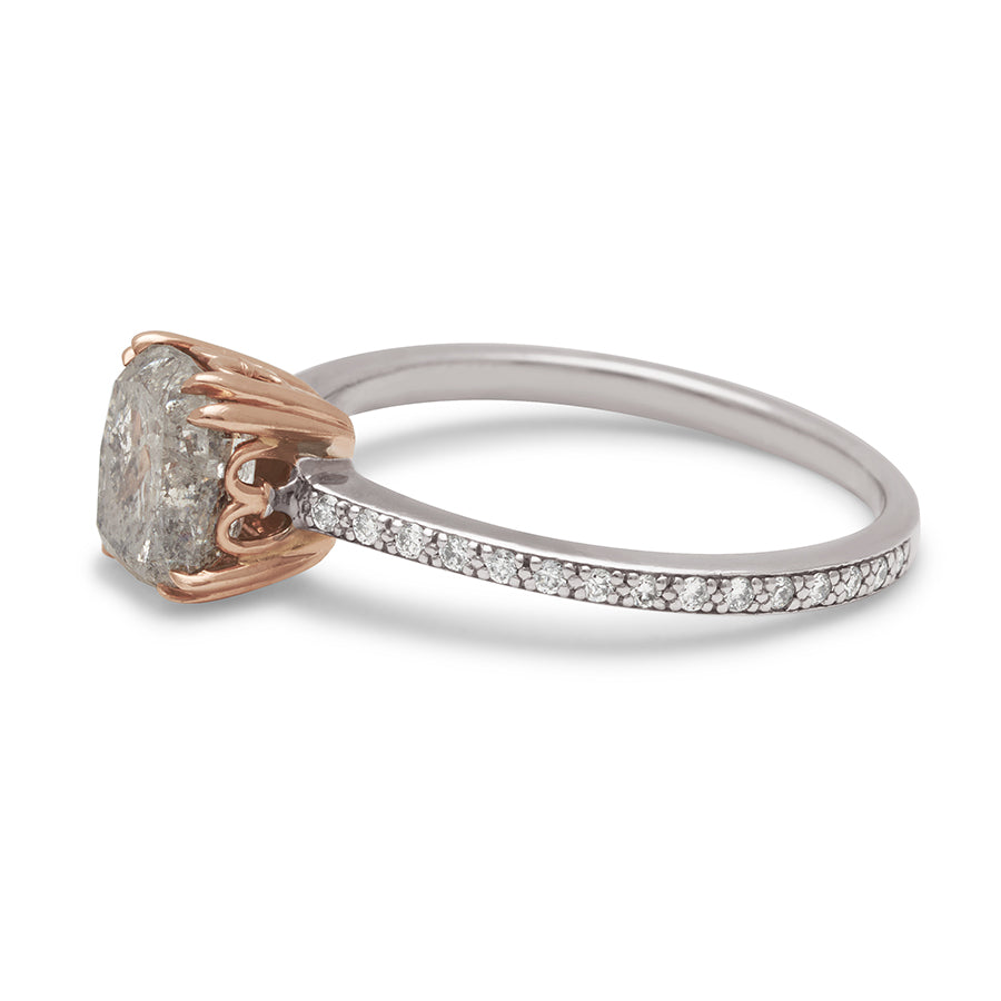 Angled view of a solitaire ring with a cushion cut grey diamond set in a rose gold basket with white diamond pave on the white gold band.