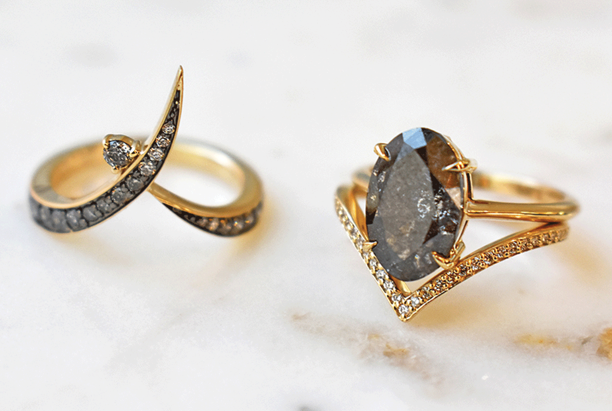 A custom bea solitaire ring with a large grey diamond oval center in 14k yellow gold paired with the diamond dusted chrysalis band.