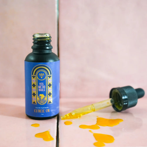 Bottle of Yes We Do Nails cuticle oil with dropper on a pink background