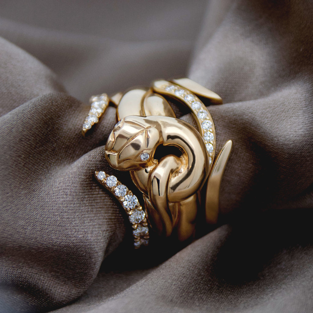 Gold serpent-shaped ring with diamond accents and other diamond and gold nesting bands on brown fabric