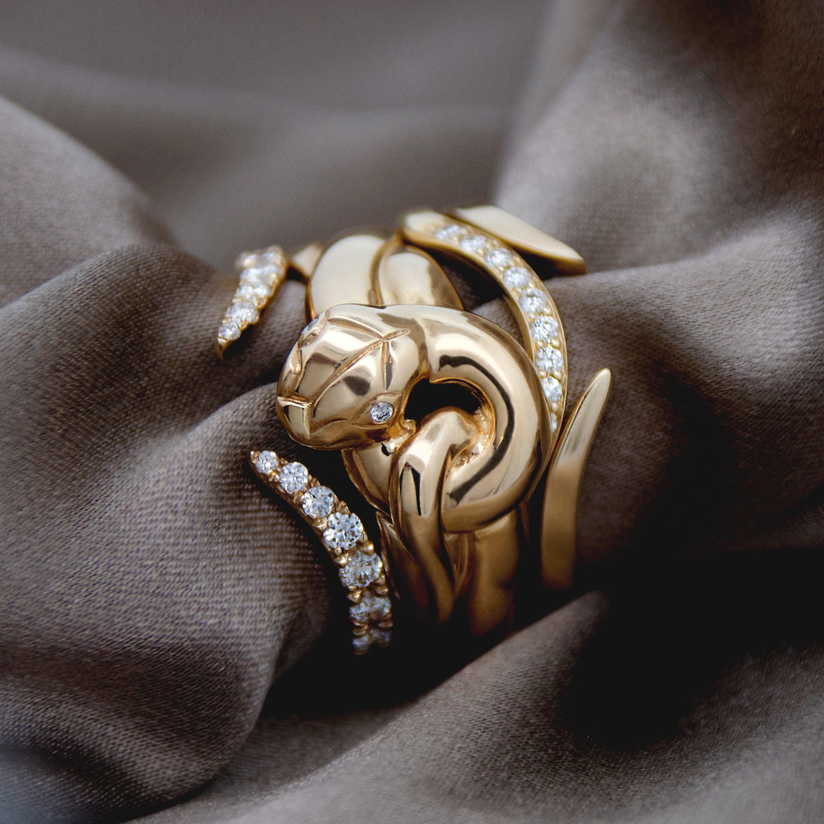 Gold serpent-shaped ring with diamond accents and other diamond and gold nesting bands on brown fabric
