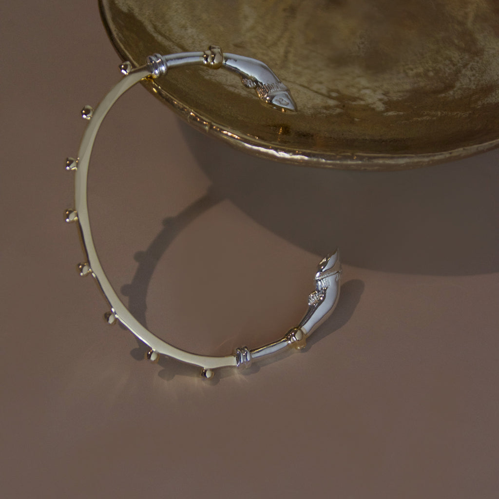 A mixed metal yellow gold and sterling silver bracelet cuff with horse hoof details against a bronze object on a beige background 