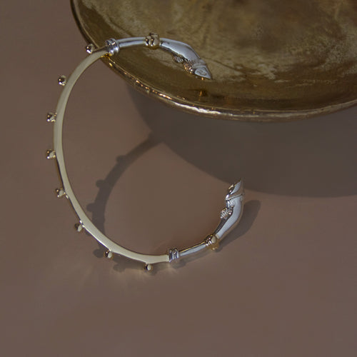 A mixed metal yellow gold and sterling silver bracelet cuff with horse hoof details against a bronze object on a beige background 