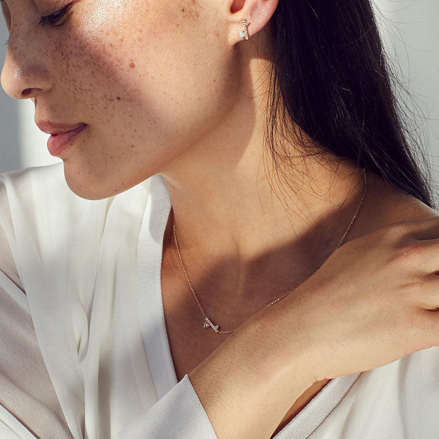 A medium-complexion model wears a diamond dusted meridian necklace with white diamonds and one stud on her ear with an opal accent stone.