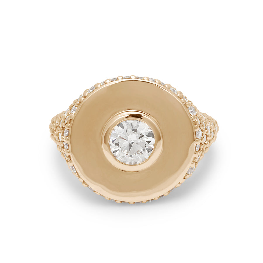 Front view of a round white diamond bezel set in a signet style ring with white diamond pave down the sides of the band set in yellow gold.