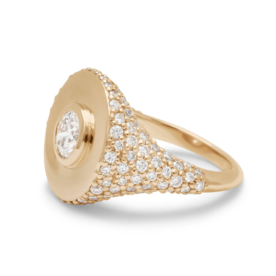 Angled view of a round white diamond bezel set in a signet style ring with white diamond pave down the sides of the band set in yellow gold.