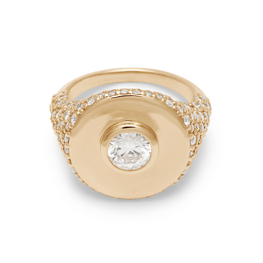 A round white diamond bezel set in a signet style ring with white diamond pave down the sides of the band set in yellow gold.