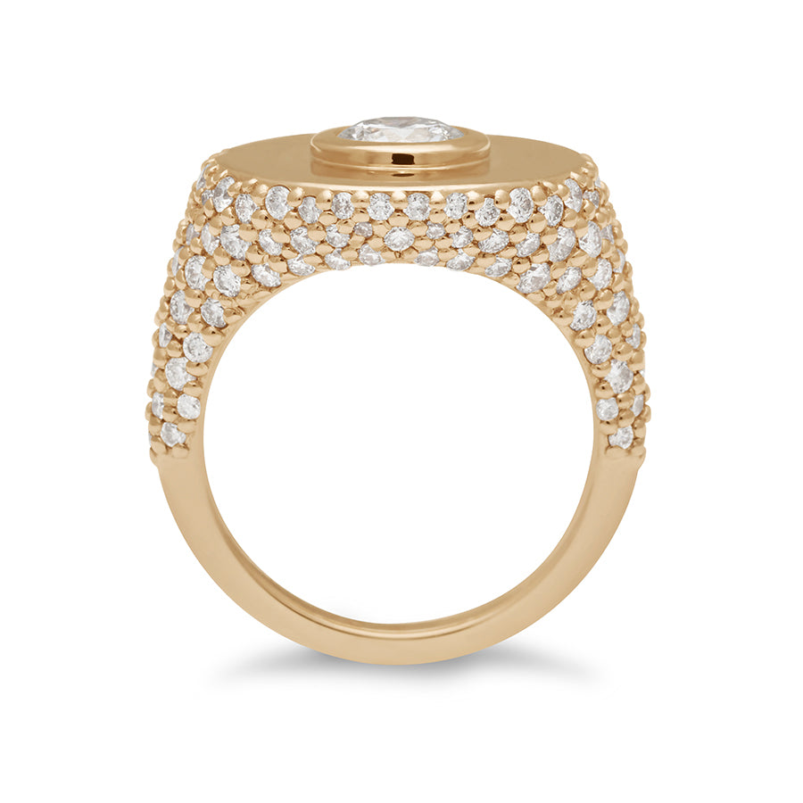 Side view of a round white diamond bezel set in a signet style ring with white diamond pave down the sides of the band set in yellow gold.