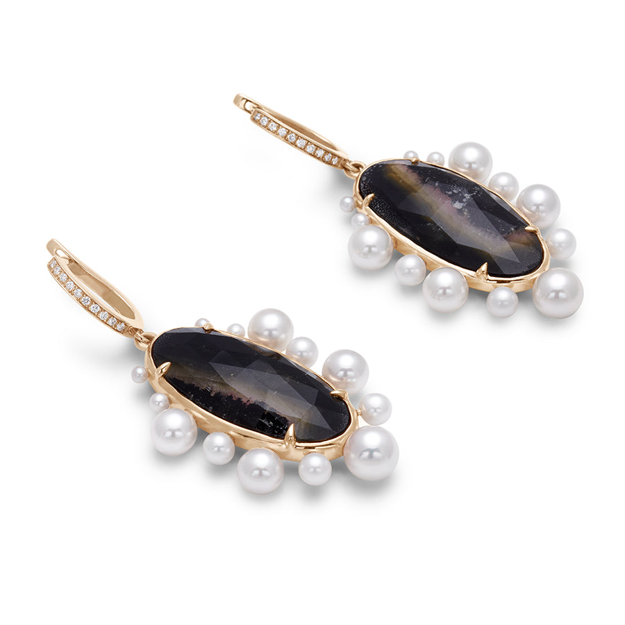 Angled view of a pair of drop hoops with an oval tourmaline stone surrounded by pearls with white diamond pave on the hoop at the top set in yellow gold.