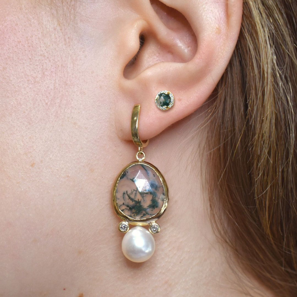 Close-up of a gold drop earring with a pearl and green moss agate gemstone drop worn by a person.