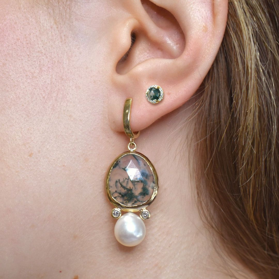 Close-up of a gold drop earring with a pearl and green moss agate gemstone drop worn by a person.