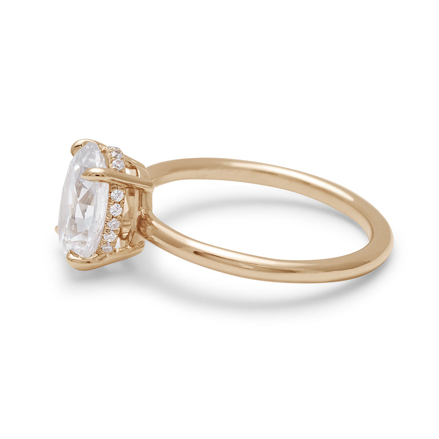 Angled view of an oval shaped lab white diamond solitaire engagement ring with a hidden white diamond pave halo under the center stone set in yellow gold.