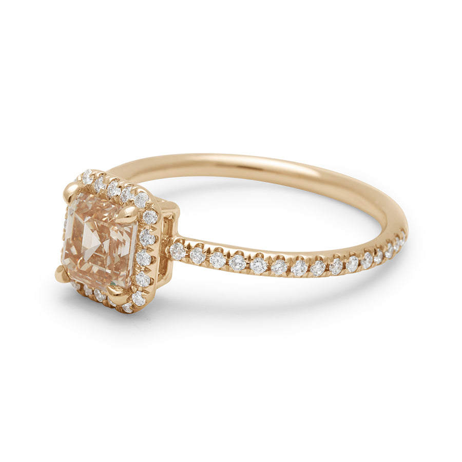 Angled view of an engagement ring with an asscher shaped champagne diamond center stone surrounded by a white diamond pave halo set in yellow gold with white diamond pave on the band.