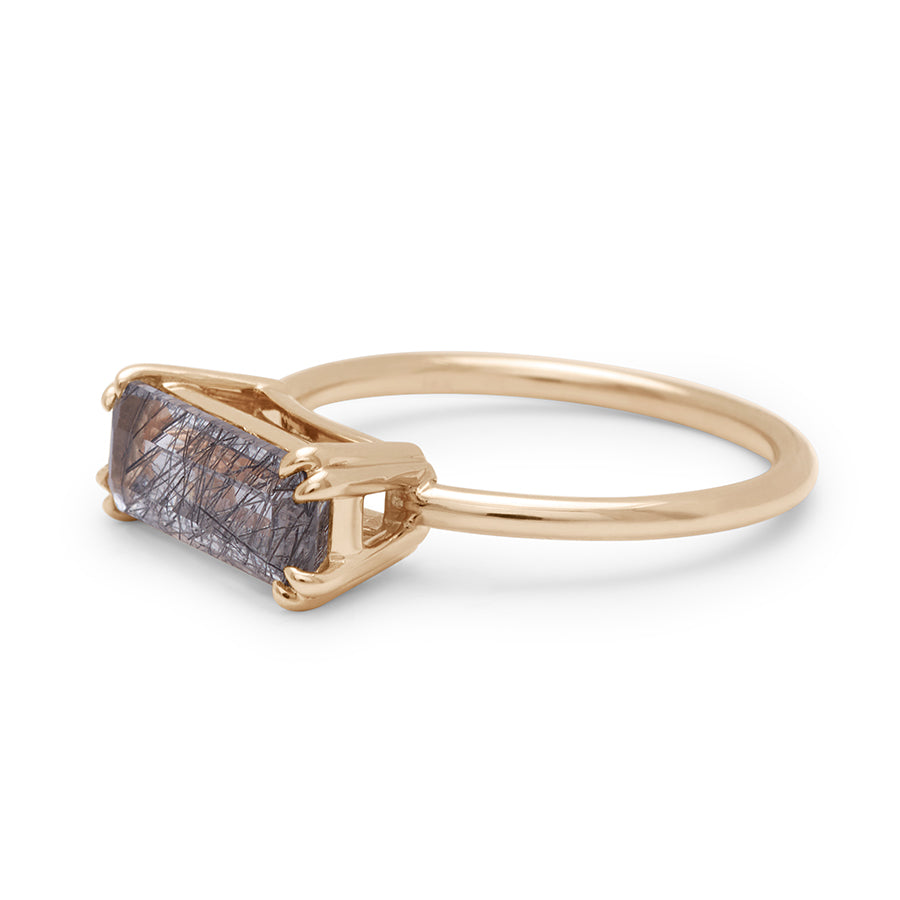 Angled view of an elongated east/west solitaire ring with an elongated emerald shape black rutilated quartz stone set in yellow gold.