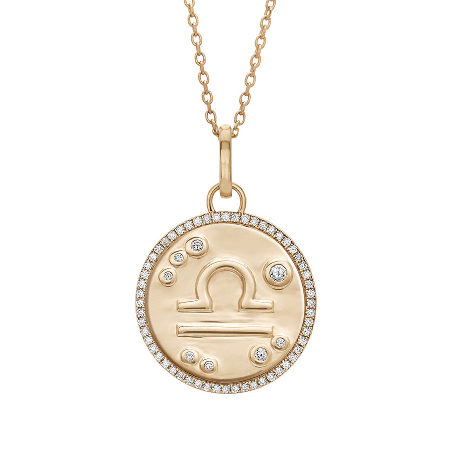 A 19mm constellation charm pendant with a Libra sign in the center with white diamond accent stones and a white diamond halo set in yellow gold on a yellow gold chain., Libra
