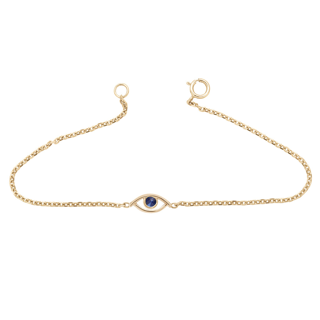 An evil eye charm with a blue sapphire stone center set in yellow gold on a yellow gold chain bracelet.