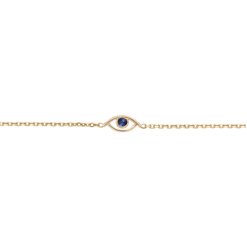 A zoomed in view of an evil eye charm with a blue sapphire stone center set in yellow gold on a yellow gold chain bracelet.