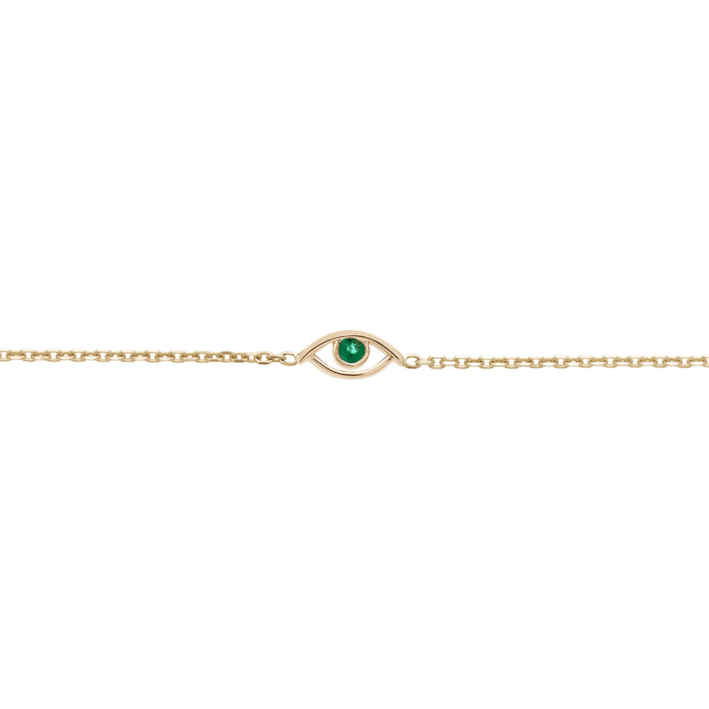 A zoomed in view of an evil eye charm with an emerald stone center set in yellow gold on a yellow gold chain bracelet.