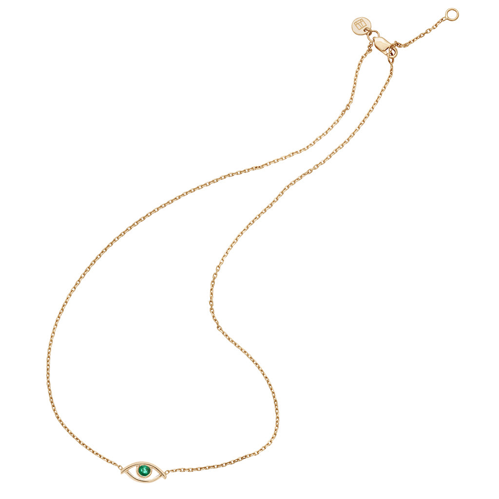 Zoomed out view of a choker with an evil eye charm with an emerald stone in the center set on a yellow gold chain with a styled curve to it.