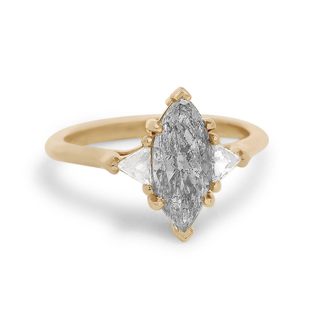 Three stone ring featuring a marquise cut grey diamond with white trillion diamond side stones set in yellow gold. 