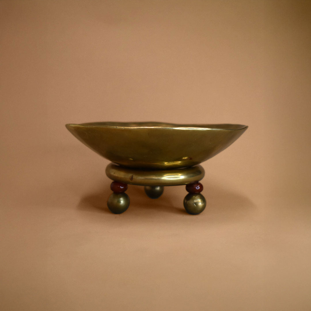 Brass bowl on a stand with red carnelian beads and bronze feet against a beige background