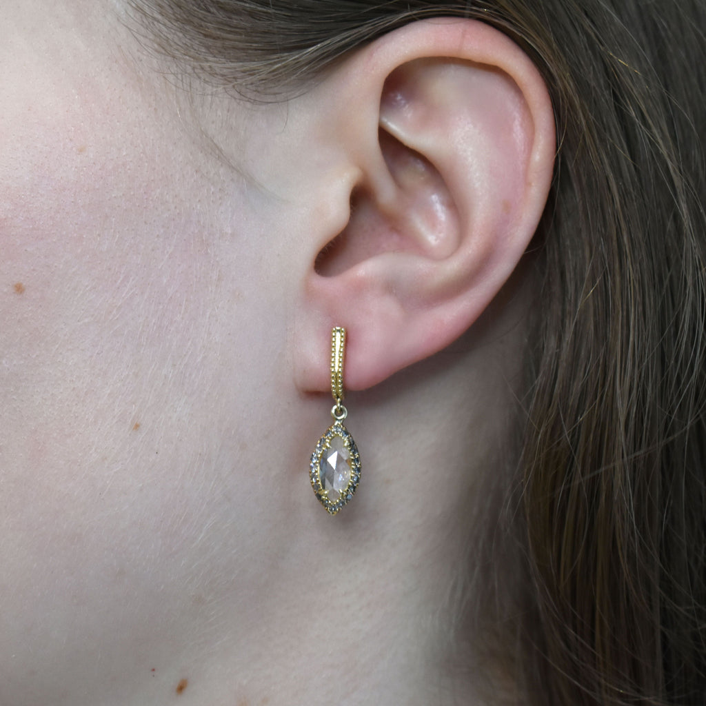 A pair of drop earrings with a U shaped hoop. One earring has white diamond pave and a marquise shaped grey diamond, the other has grey diamond pave and a marquise shaped white diamond set in yellow gold one earring angled.