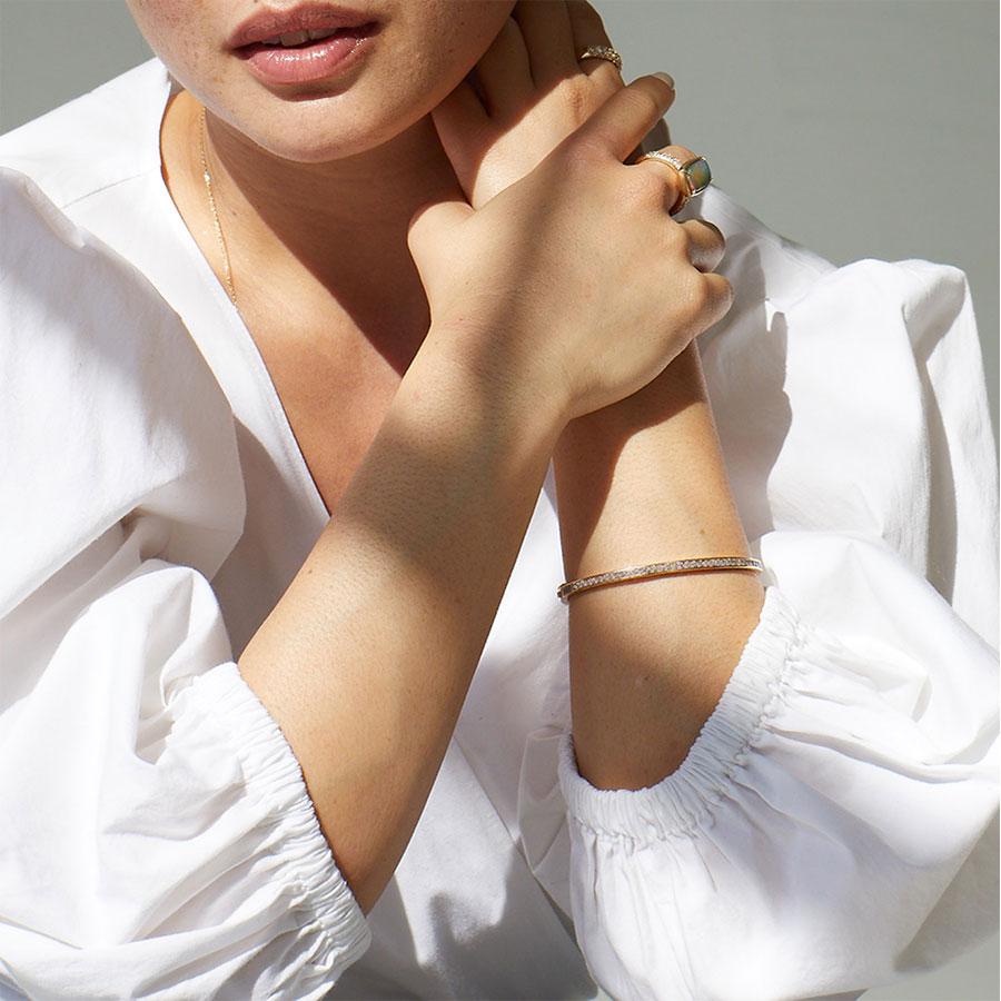 A bracelet with a line of champagne diamonds set around the band set in yellow gold on the wrist of a light-complexion model.