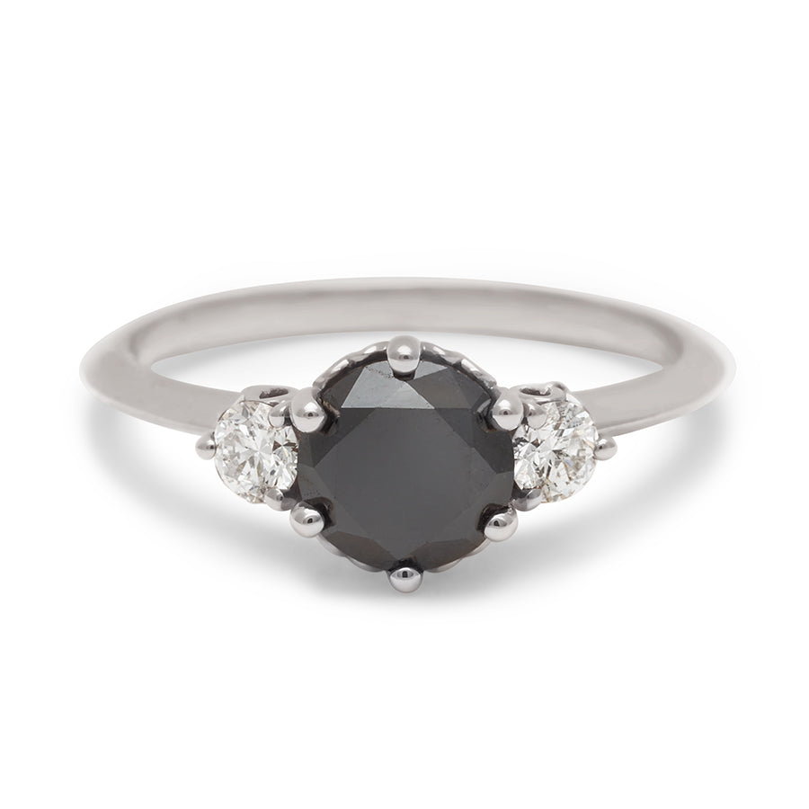 A three stone engagement ring with a round shape black diamond center stone with two white diamond round side stones set in white gold., White Gold