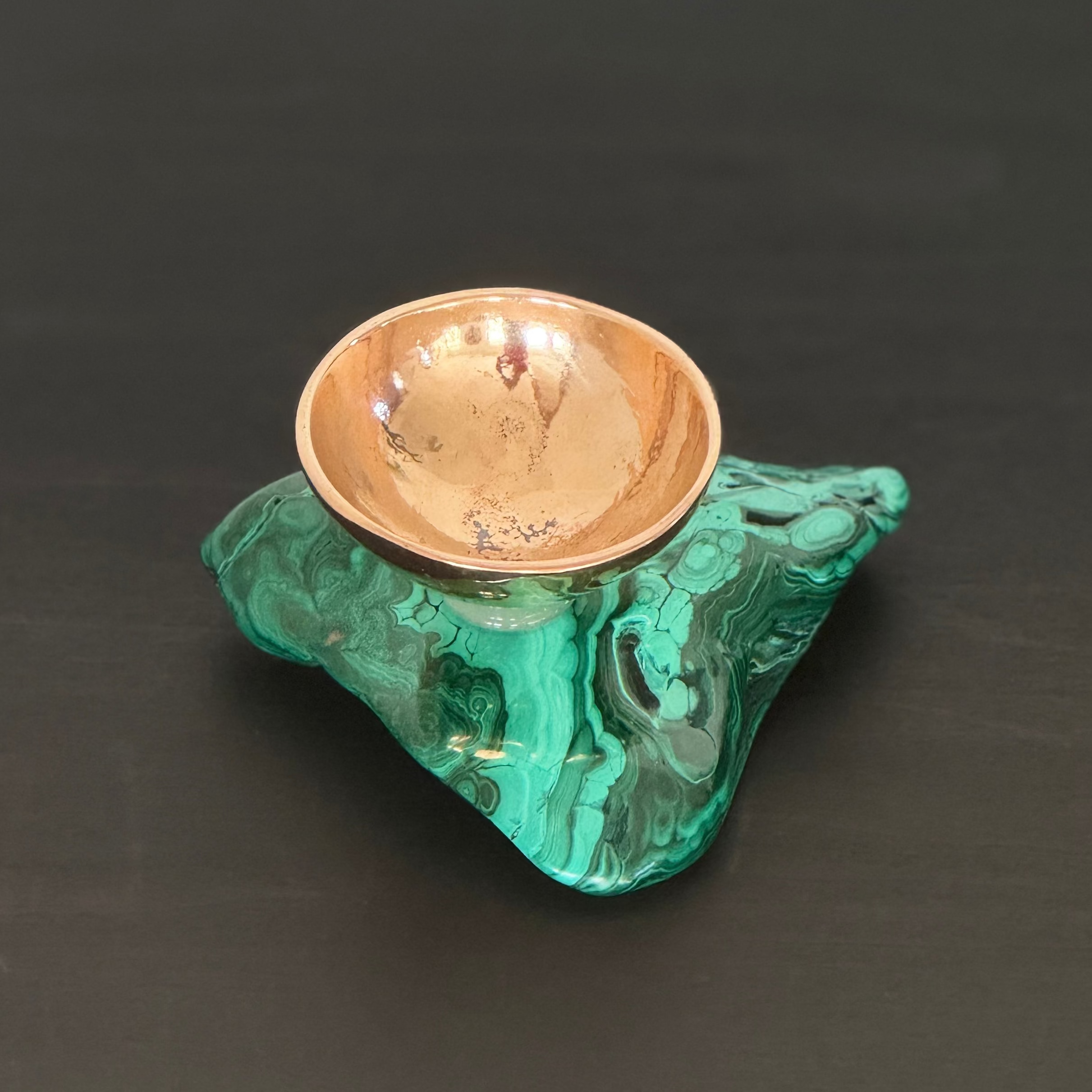 Small bronze bowl on a green malachite stone base against a black background
