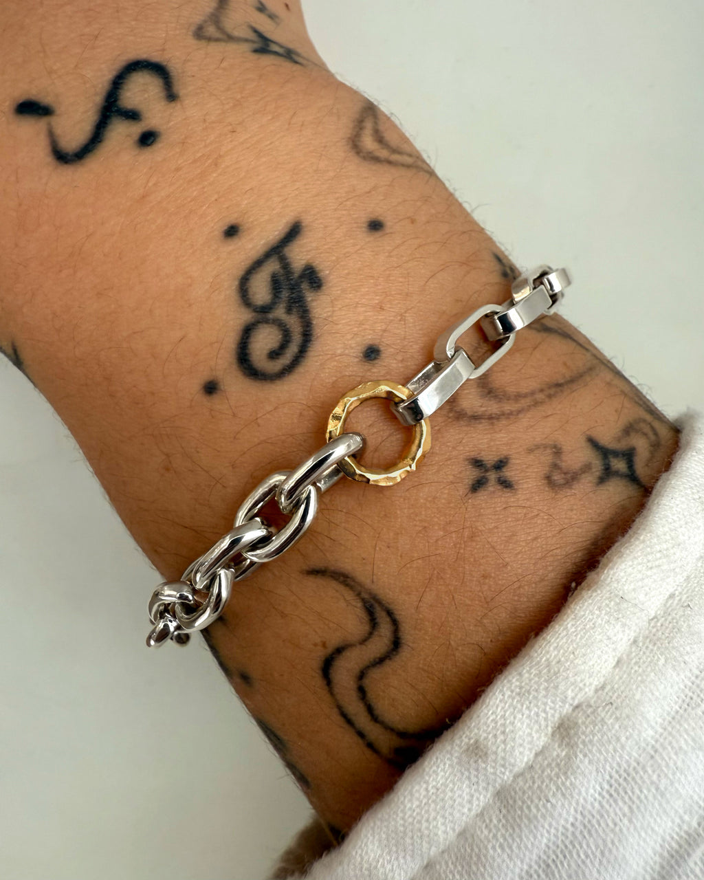 A silver chain bracelet with a yellow gold hoop detail worn on-figure on a person's wrist. 