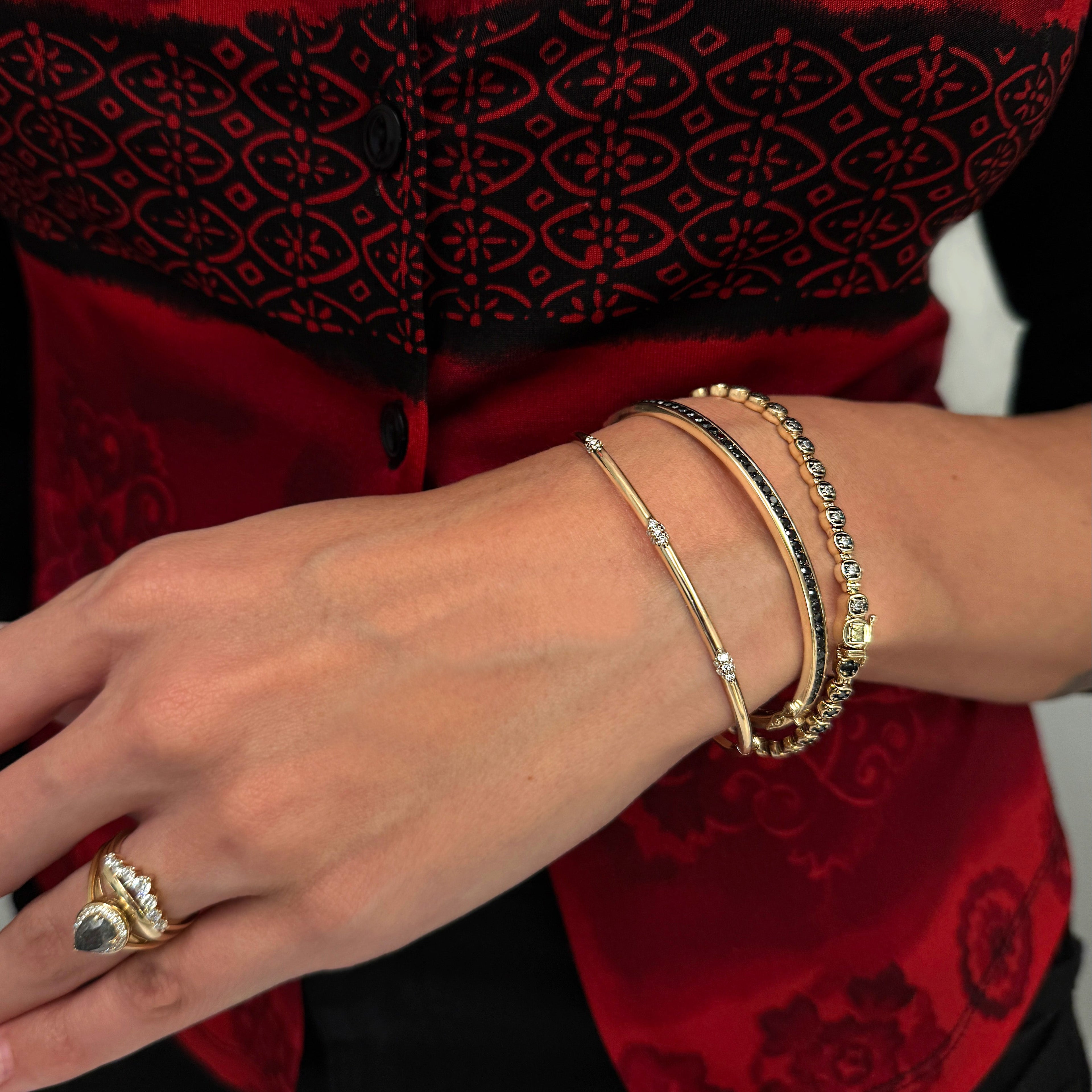 A photo of a woman wearing three gold bracelets and a red shirt 