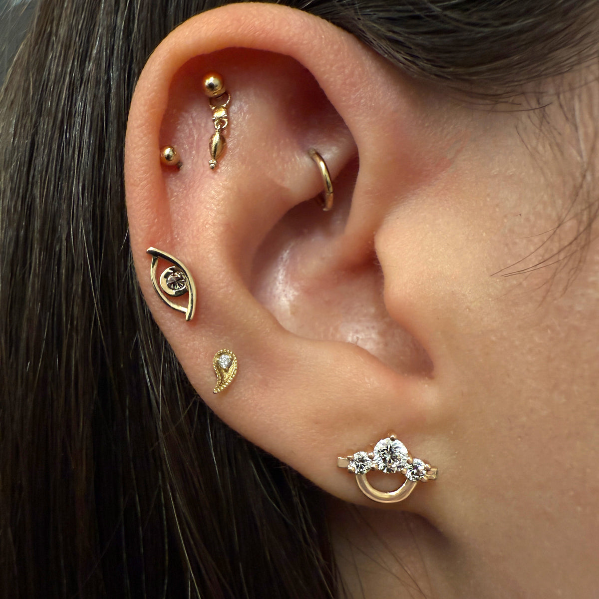 Close-up of a person's ear showcasing multiple gold and silver cartilage piercings and stud earrings.
