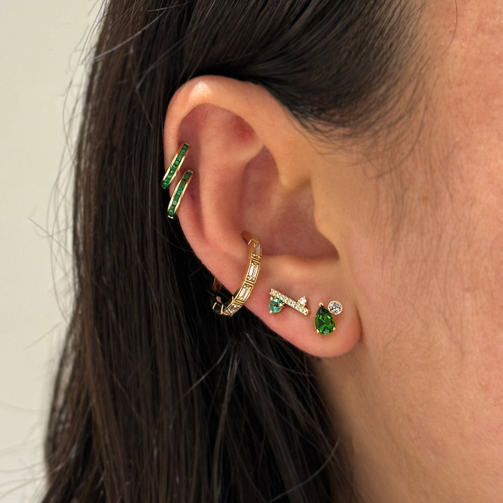 A close-up of an ear wearing multiple gold and green gemstone earrings 