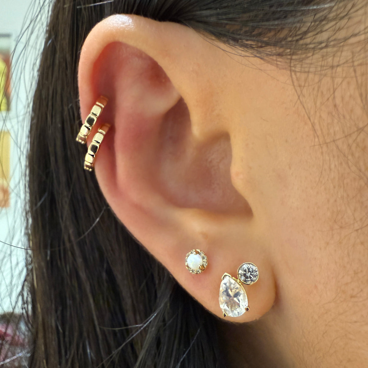 Close-up of a person's ear showcasing a multi-piece gold ear cuff and stud earrings, with dark hair framing the side of the face.