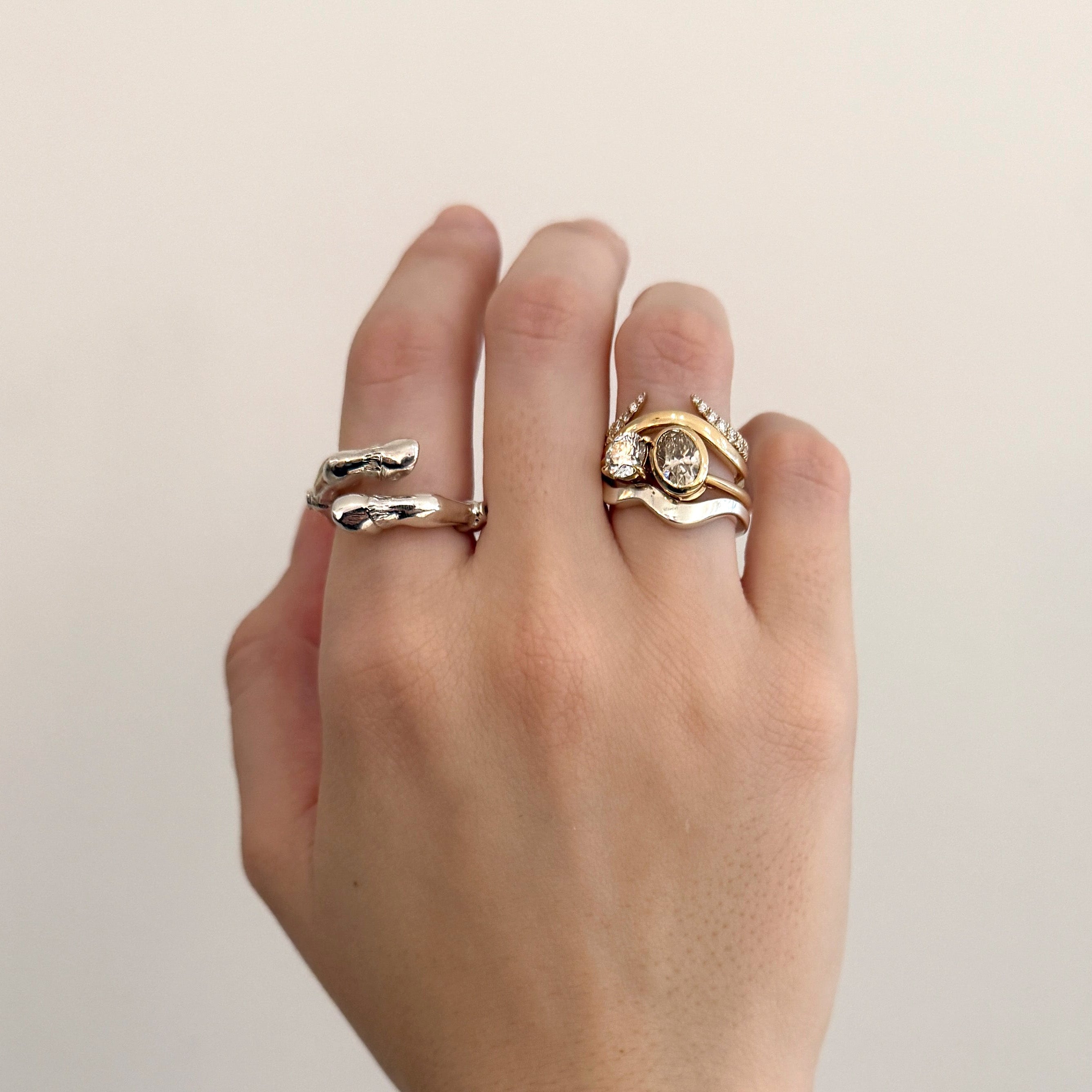 A hand wearing silver and gold rings against a grey background