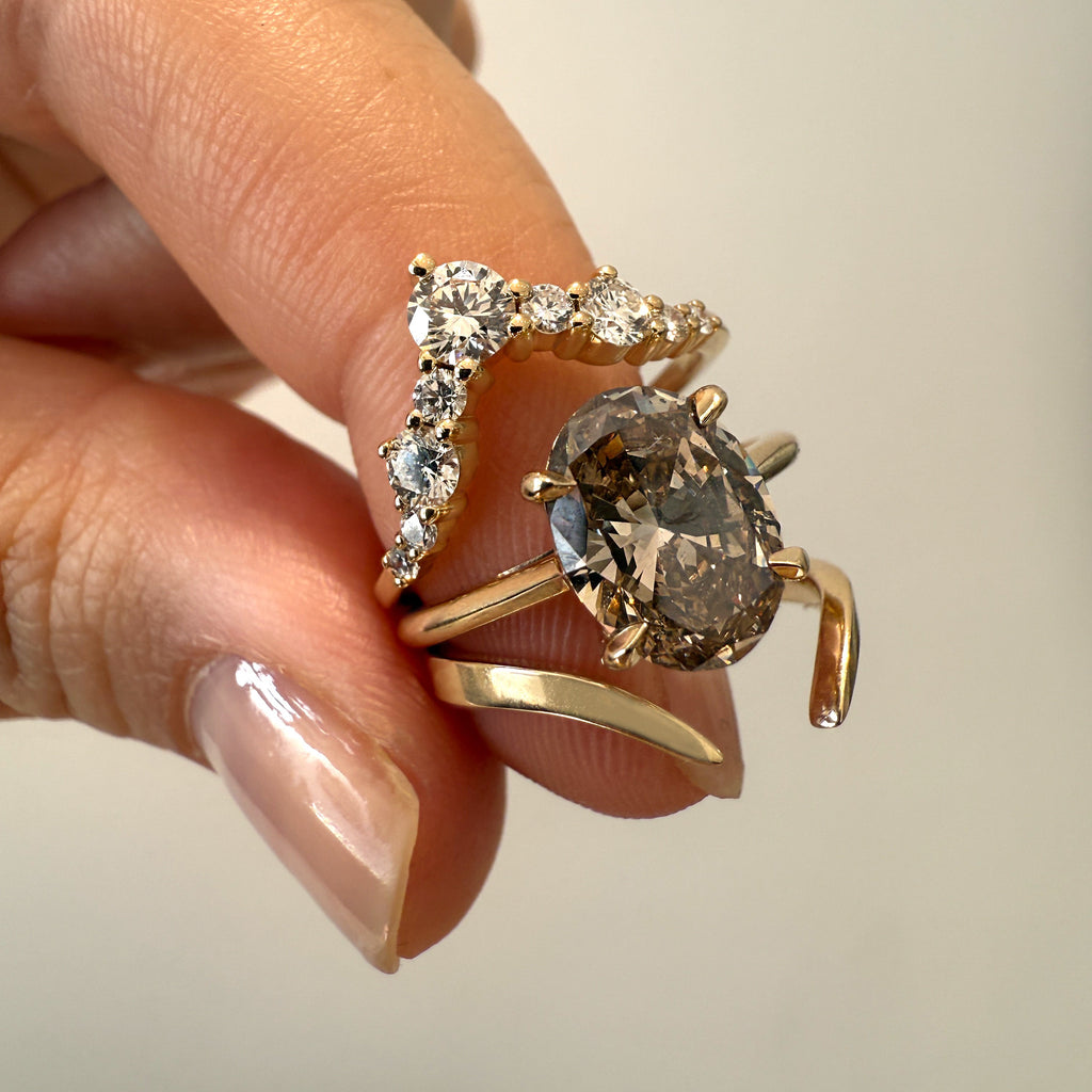 Two gold rings with gemstones held by a hand against a neutral background