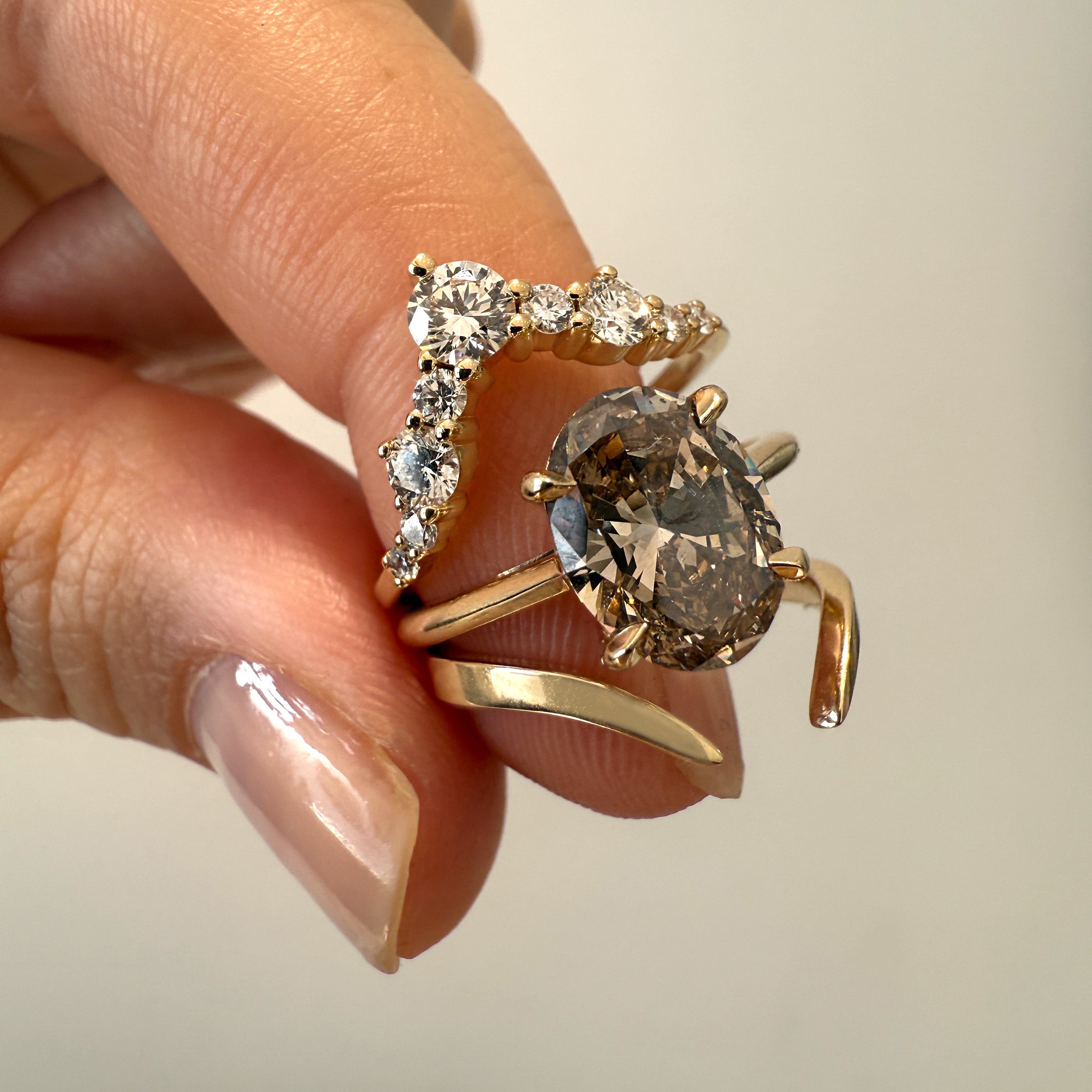 Two gold rings with gemstones held by a hand against a neutral background