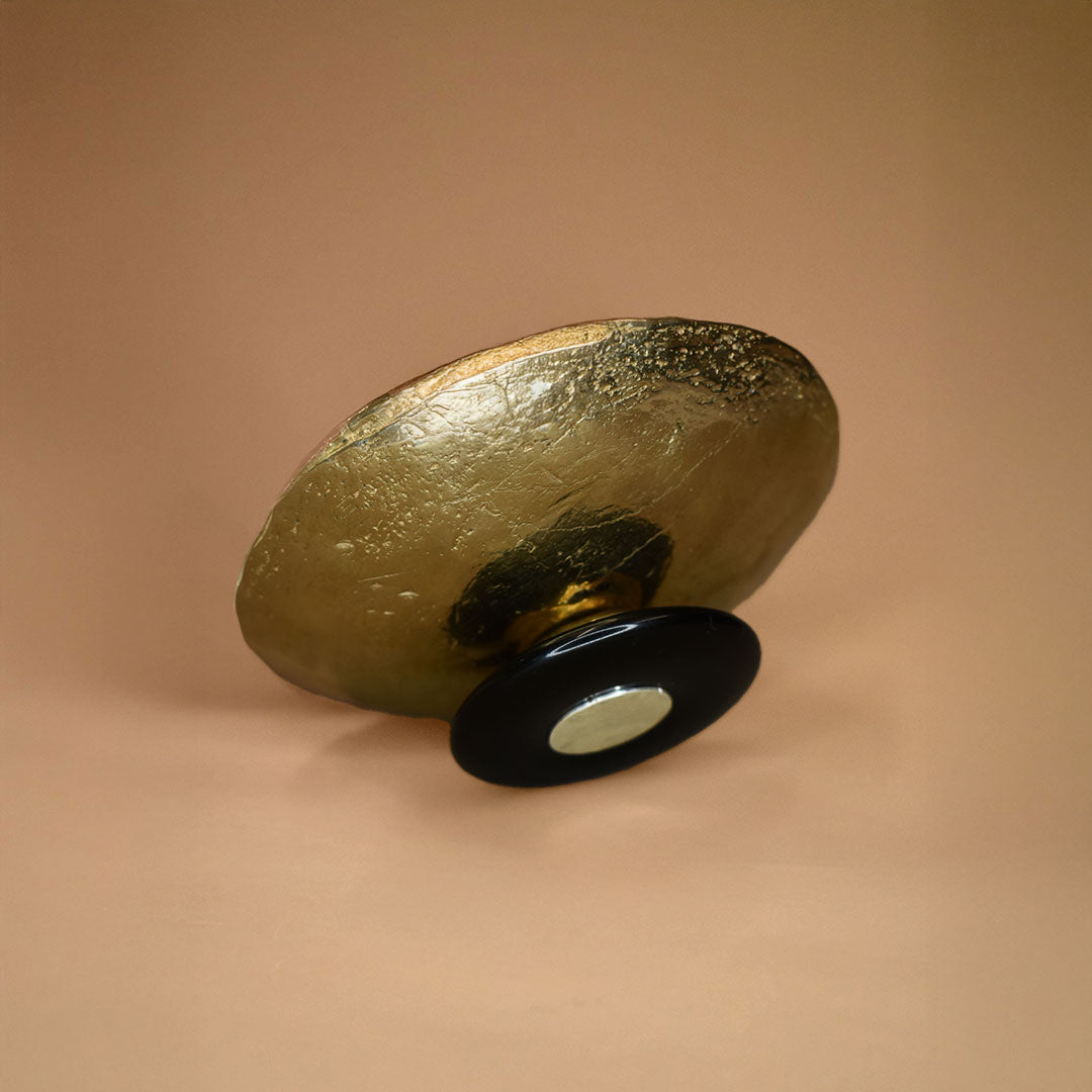 A bronze dish with a black jasper base on its side on a beige background