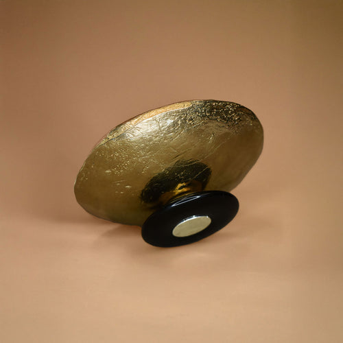 A bronze dish with a black jasper base on its side on a beige background