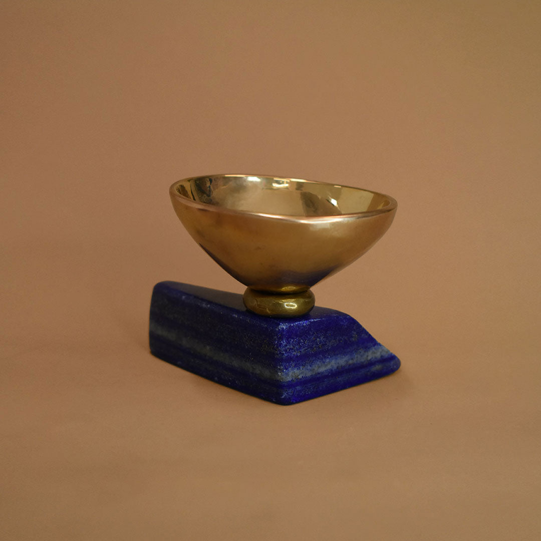 Bronze bowl adhered to a slab of lapis lazuli on a beige background