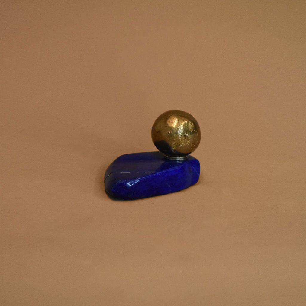 Small bronze ball adhered to a piece of lapis lazuli on a beige background