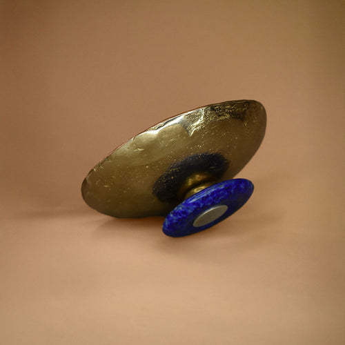 Bronze dish with lapis lazuli base on its side on a beige background