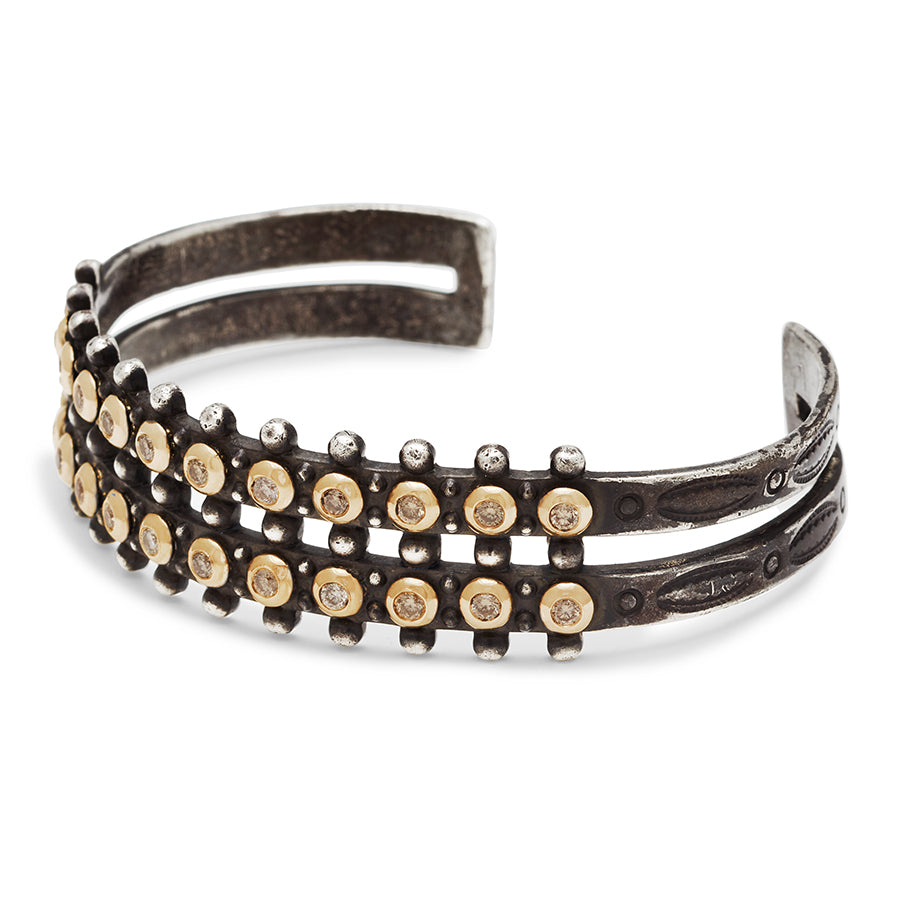 Angled view of a sterling silver cuff with two rows of champagne diamonds bezel set in yellow gold.