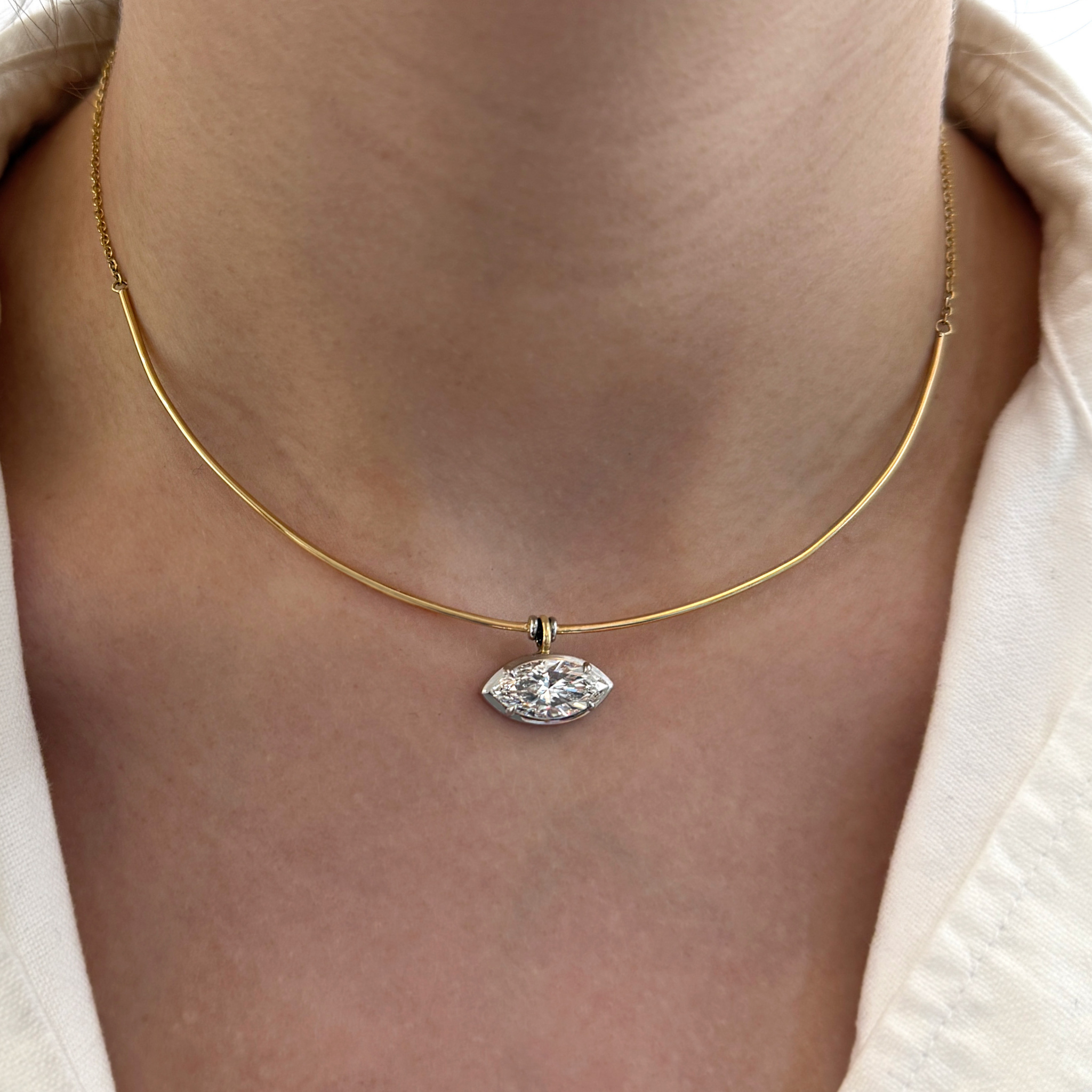 Gold necklace with a diamond pendant on a person wearing a beige top.