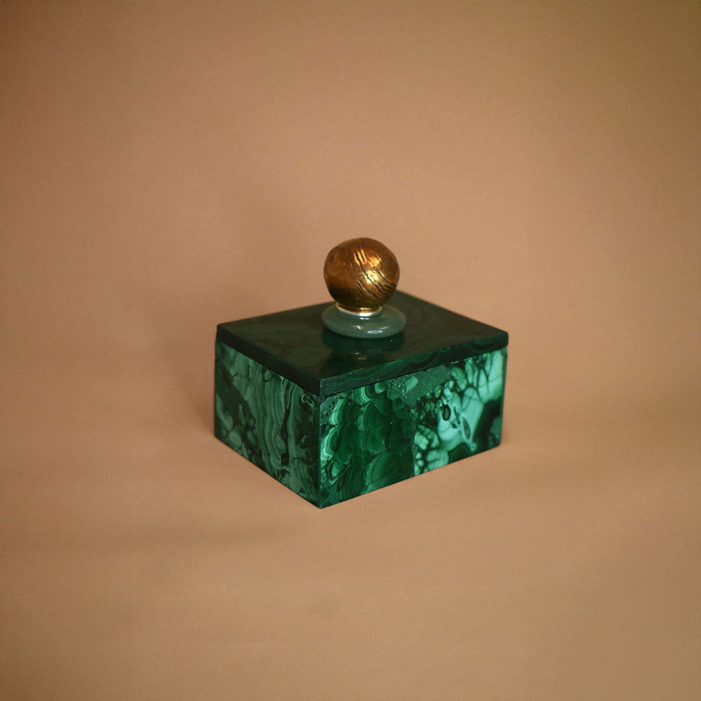 Malachite box with an Aventurine gemstone and bronze ball on top of lid on a beige background