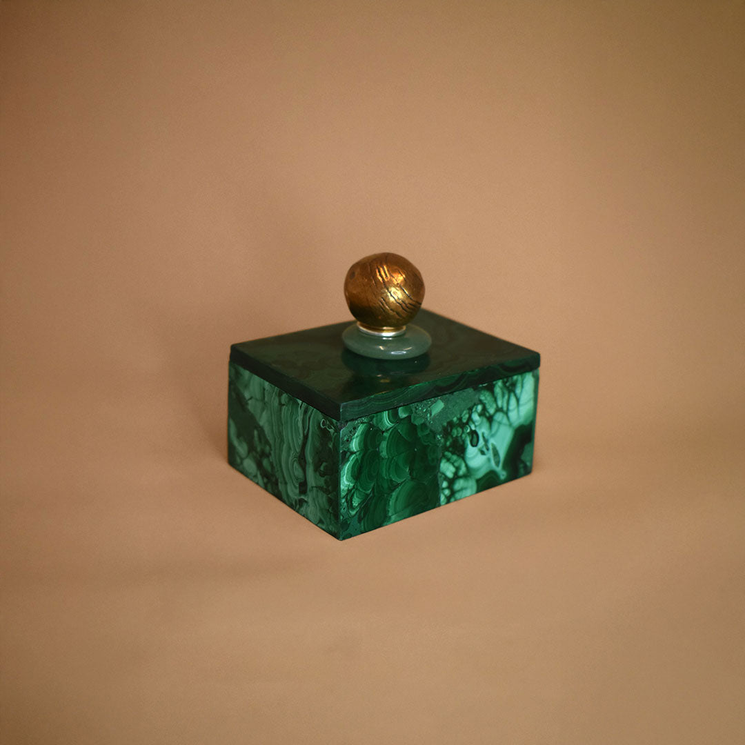 Malachite box with an Aventurine gemstone and bronze ball on top of lid on a beige background