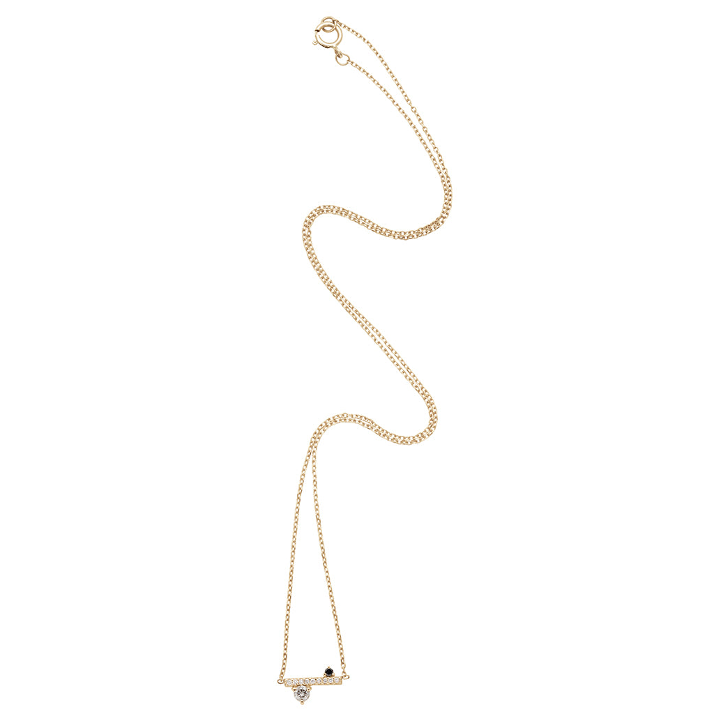 A zoomed out view of a straight line of white diamond pave with grey and black diamond accent stones on either side set in a yellow gold necklace chain.
