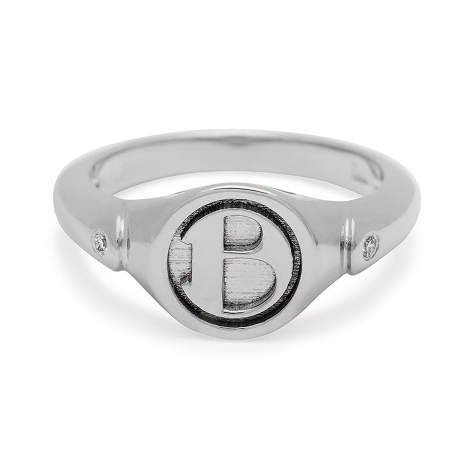 A monogrammed signet ring with a "B" on the front and two grey diamond accents on either side and set in sterling silver.