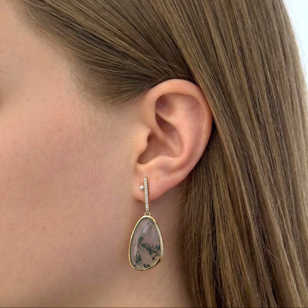 Woman wearing a gold earring with a teardrop-shaped gemstone in a store setting