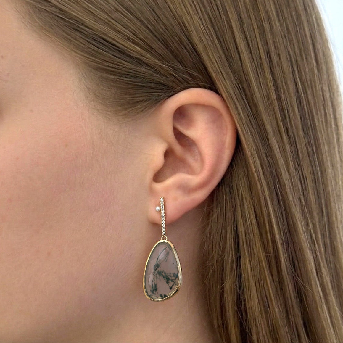 Woman wearing a gold earring with a teardrop-shaped gemstone in a store setting